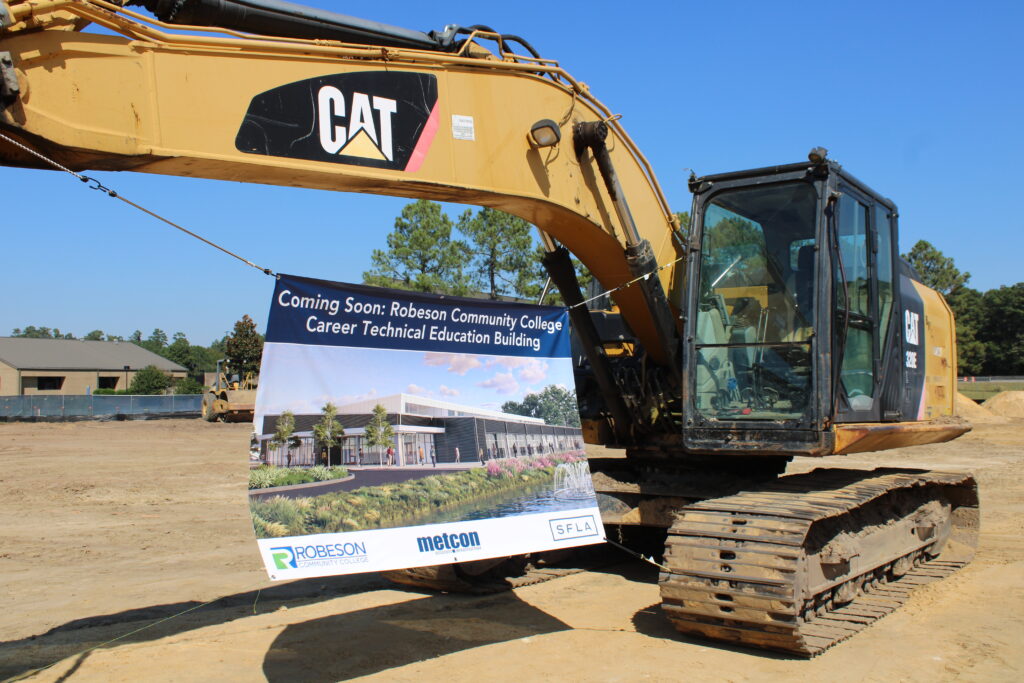 backhoe holding up banner of the image of the new career technical education building