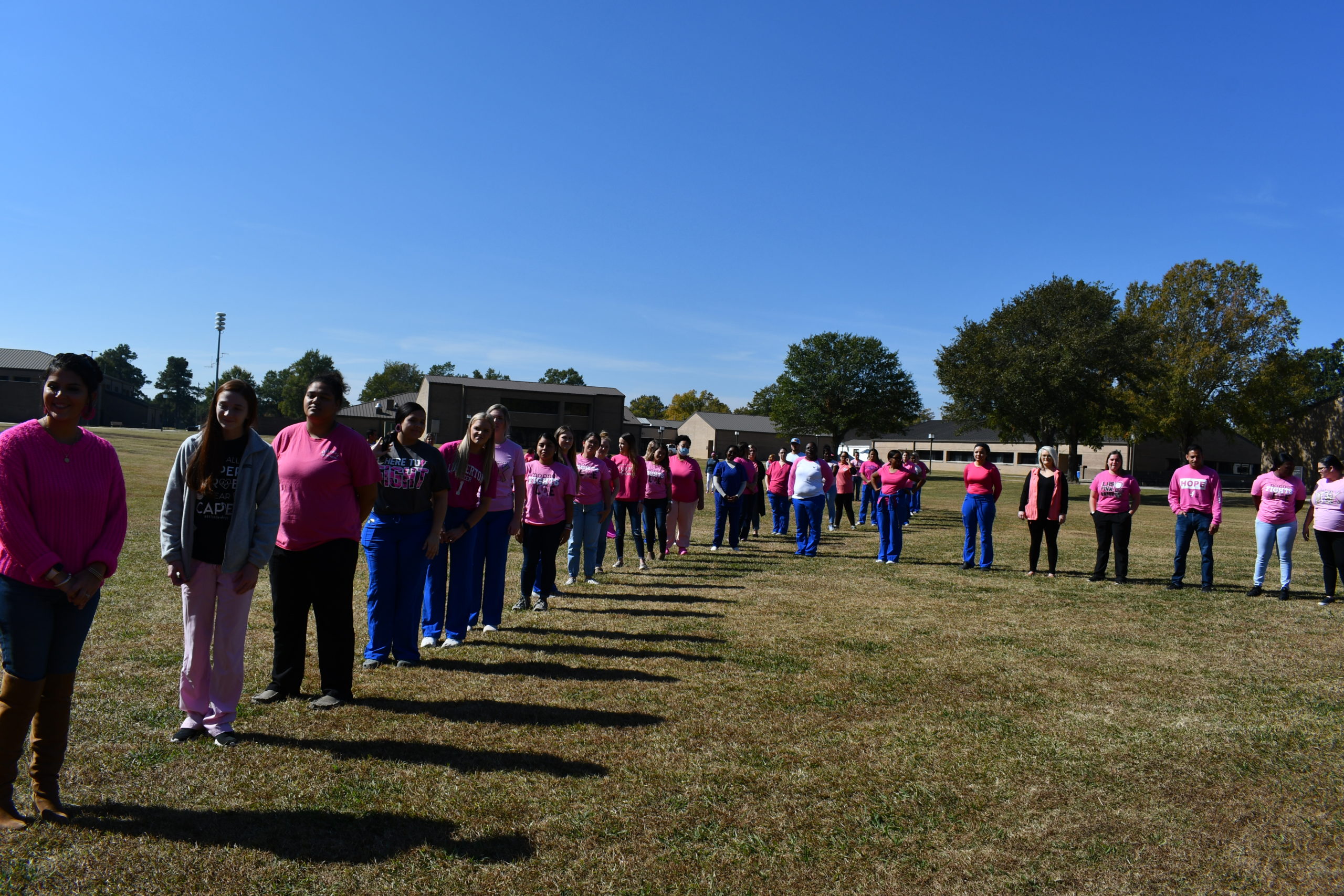 Nursing students stand to make a human pink ribbon in middle of campus