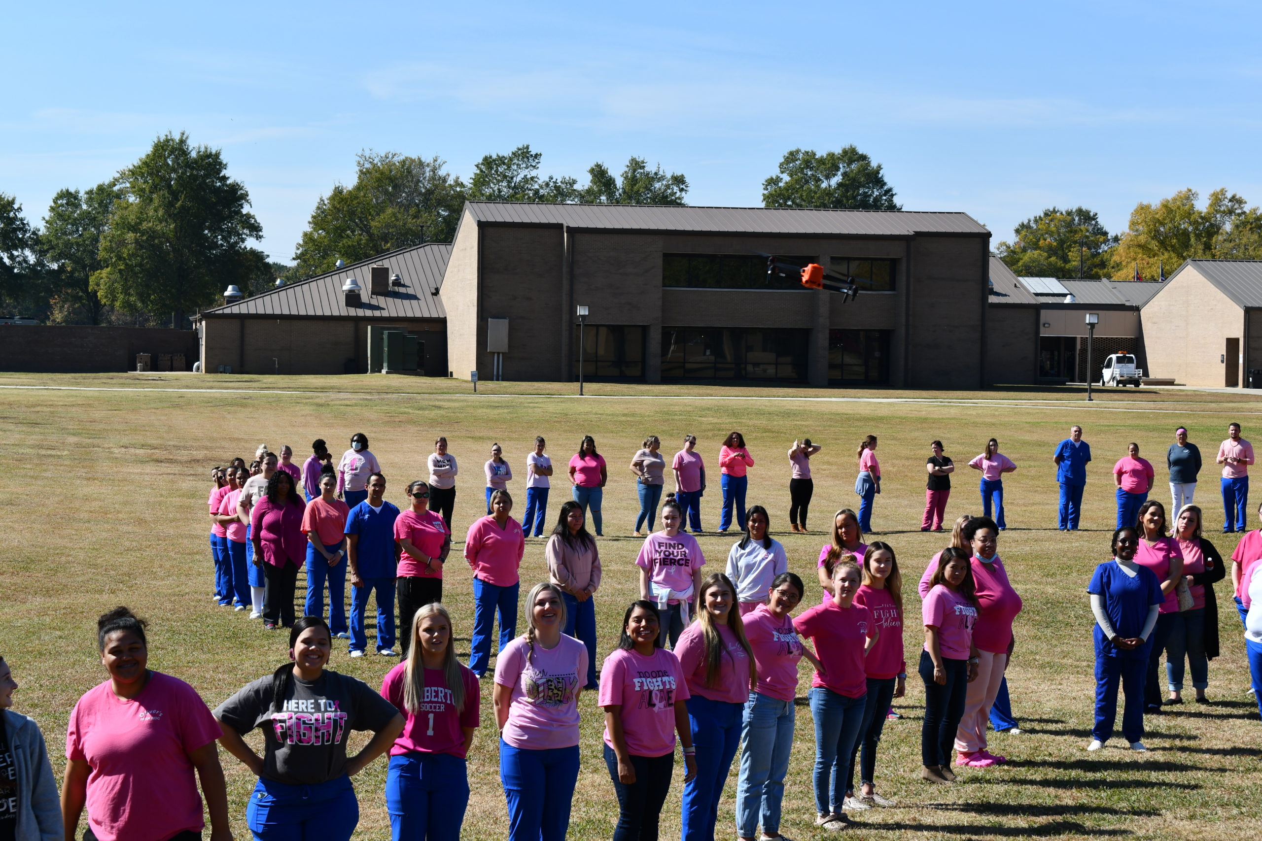 Nursing students stand to make a human pink ribbon in middle of campus