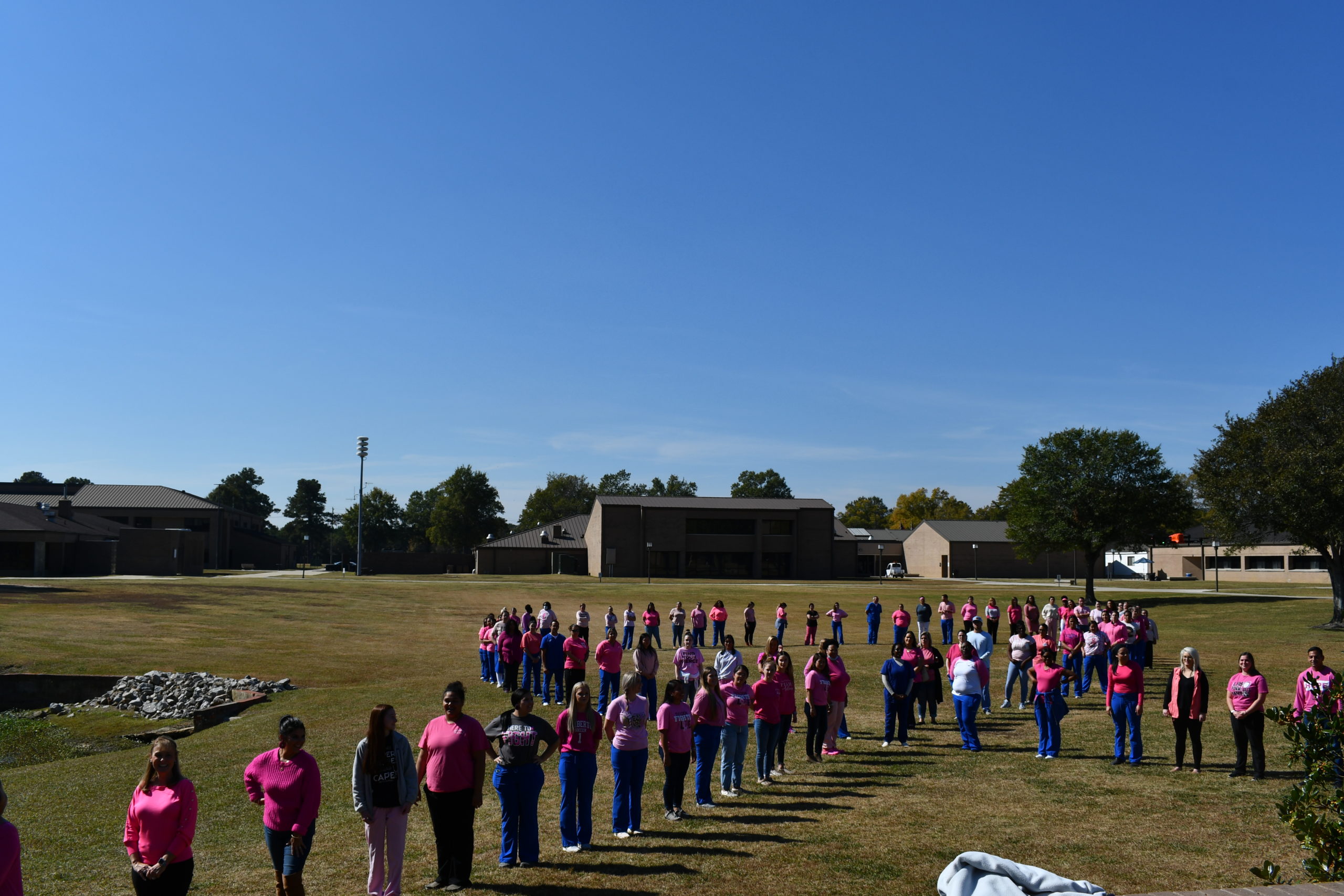 Nursing students stand to make a human pink ribbon in middle of campus