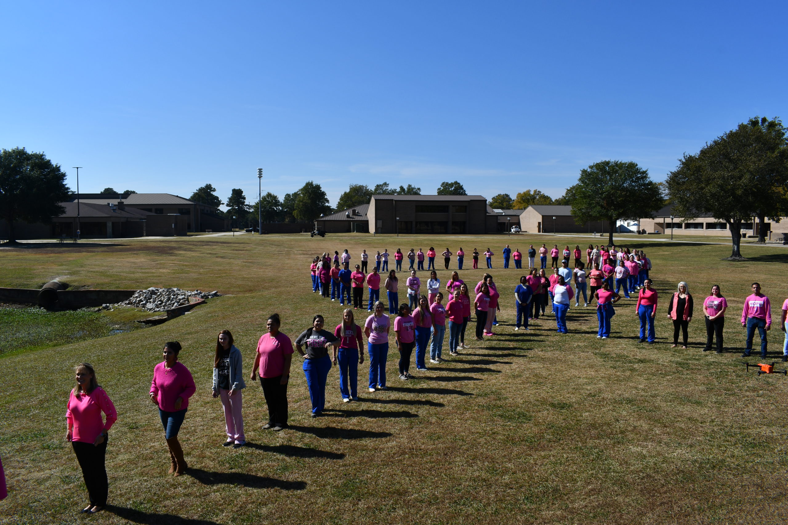 Nursing students stand to make a human pink ribbon in middle of campus
