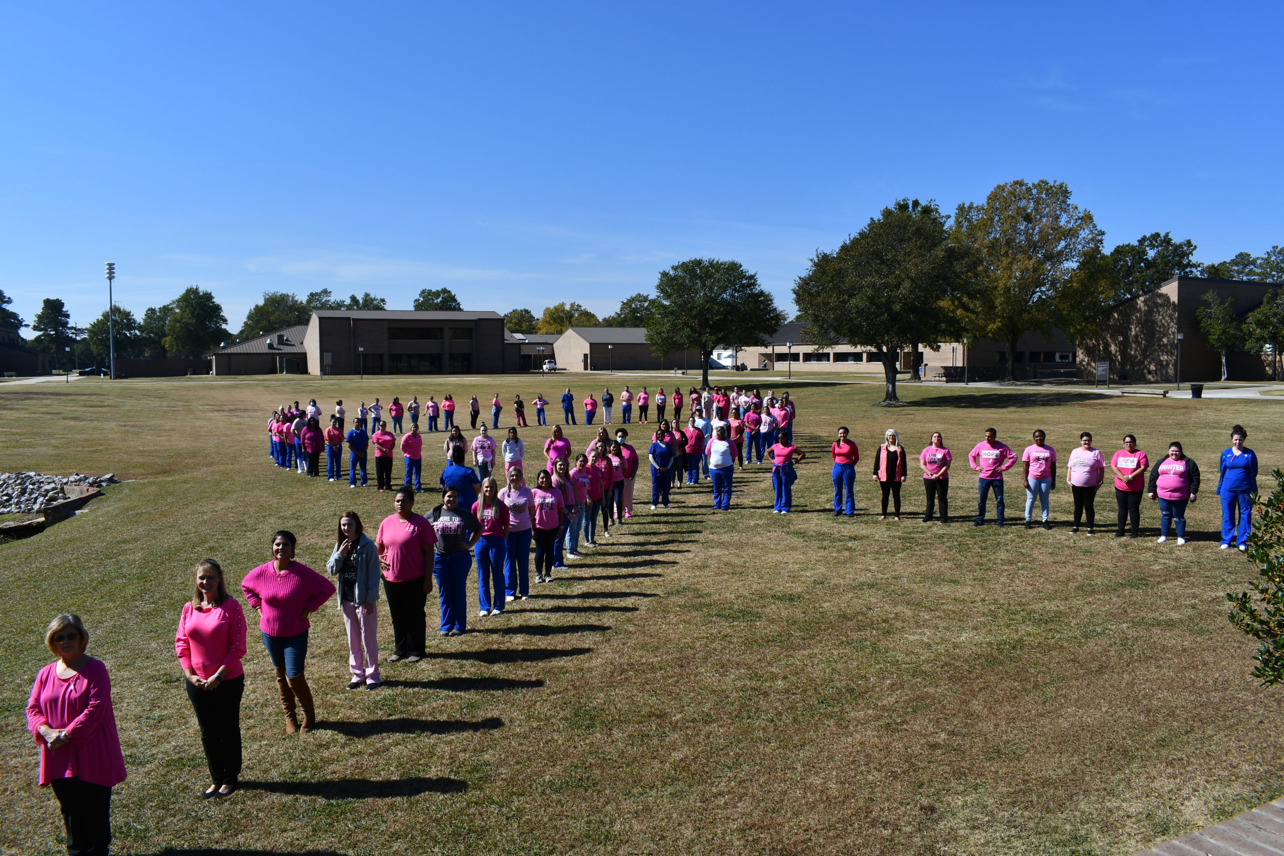 Nursing students stand to make a human pink ribbon in middle of campus