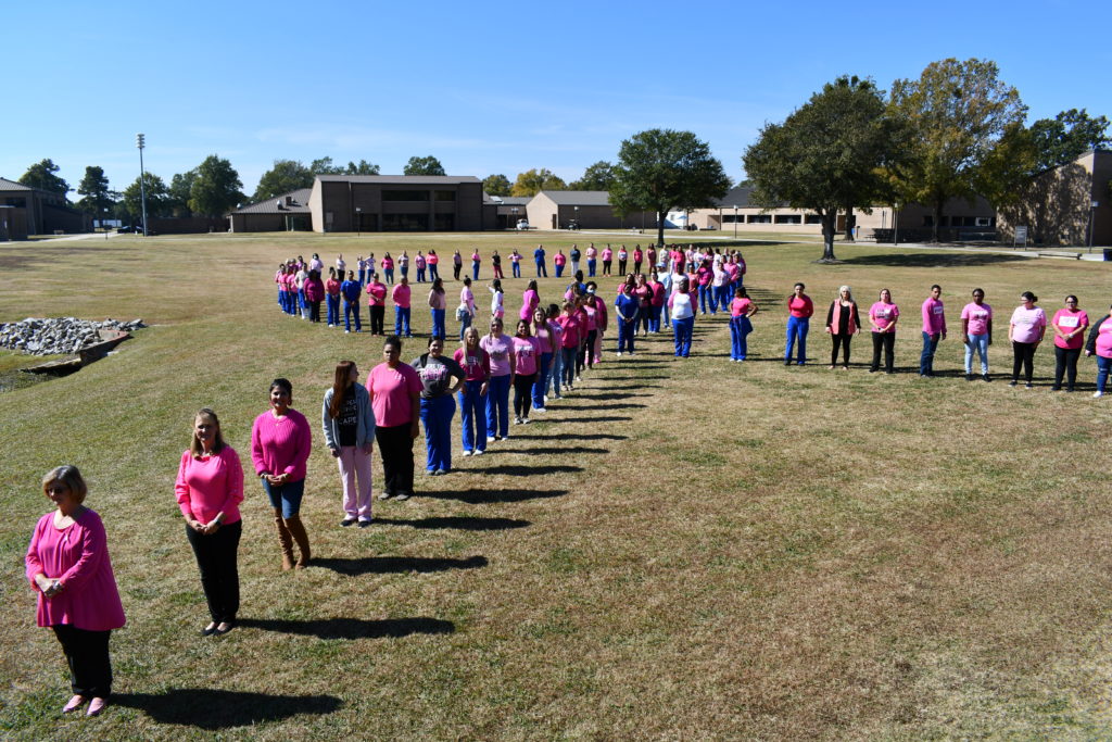 Nursing students stand to make a human pink ribbon in middle of campus