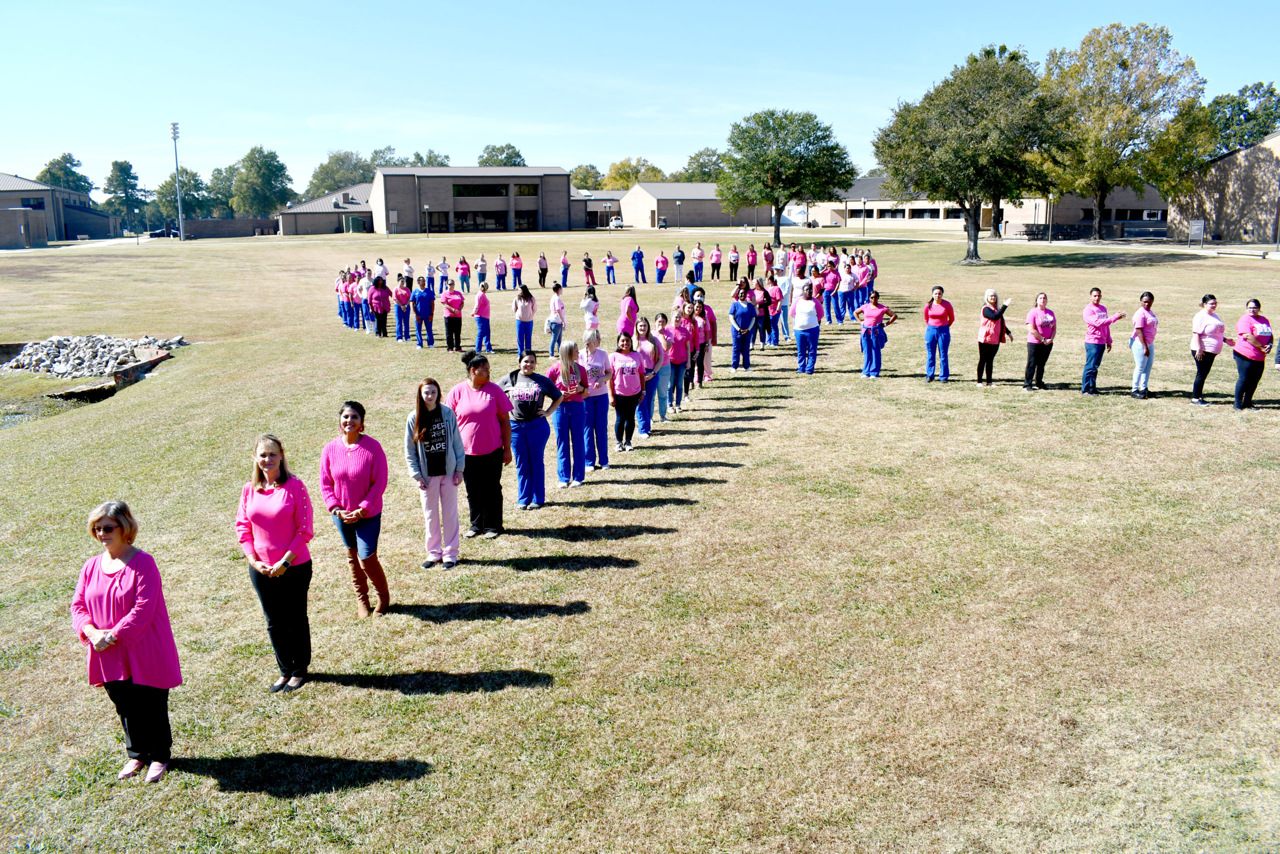 Nursing students stand to make a human pink ribbon in middle of campus