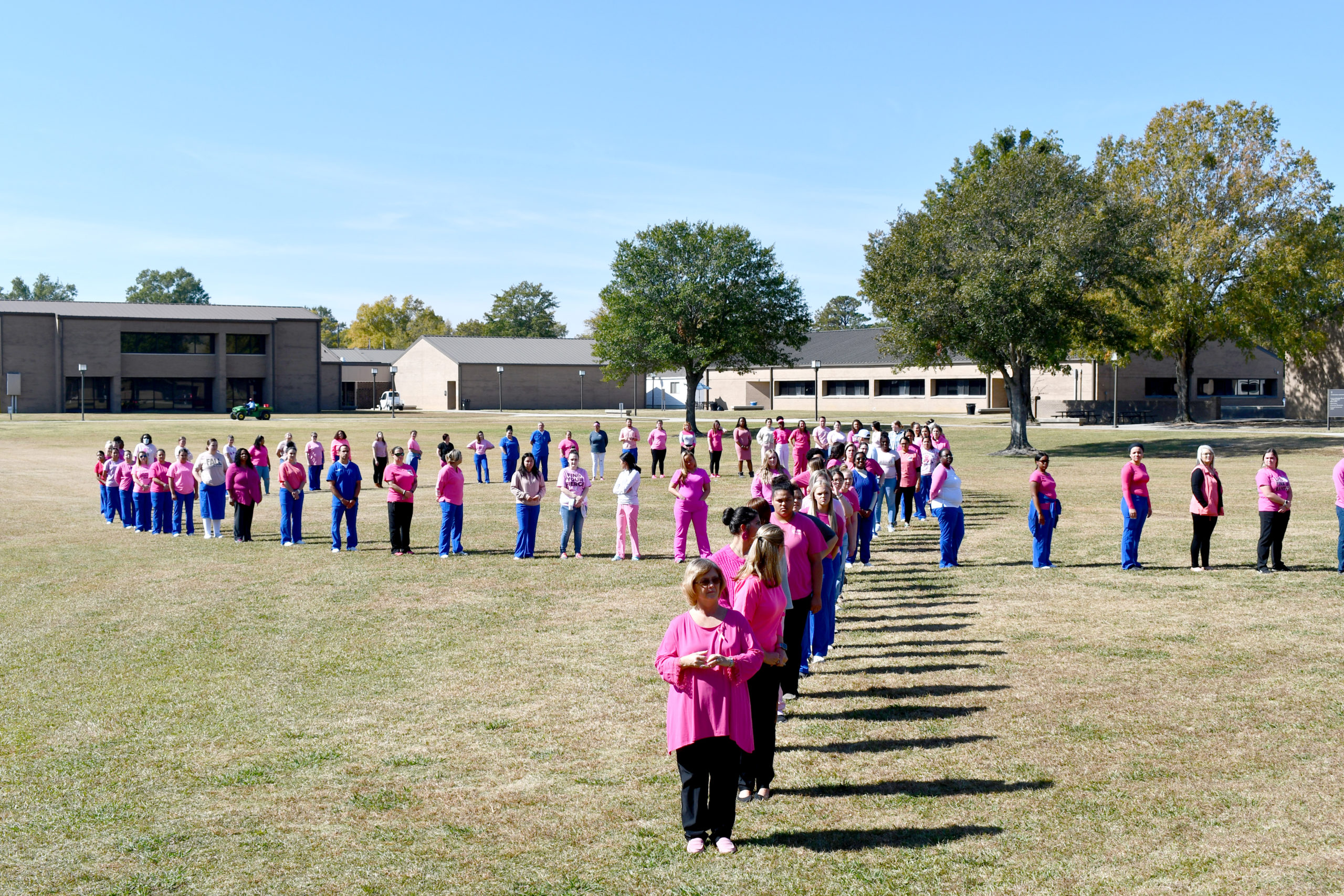 Nursing students stand to make a human pink ribbon in middle of campus