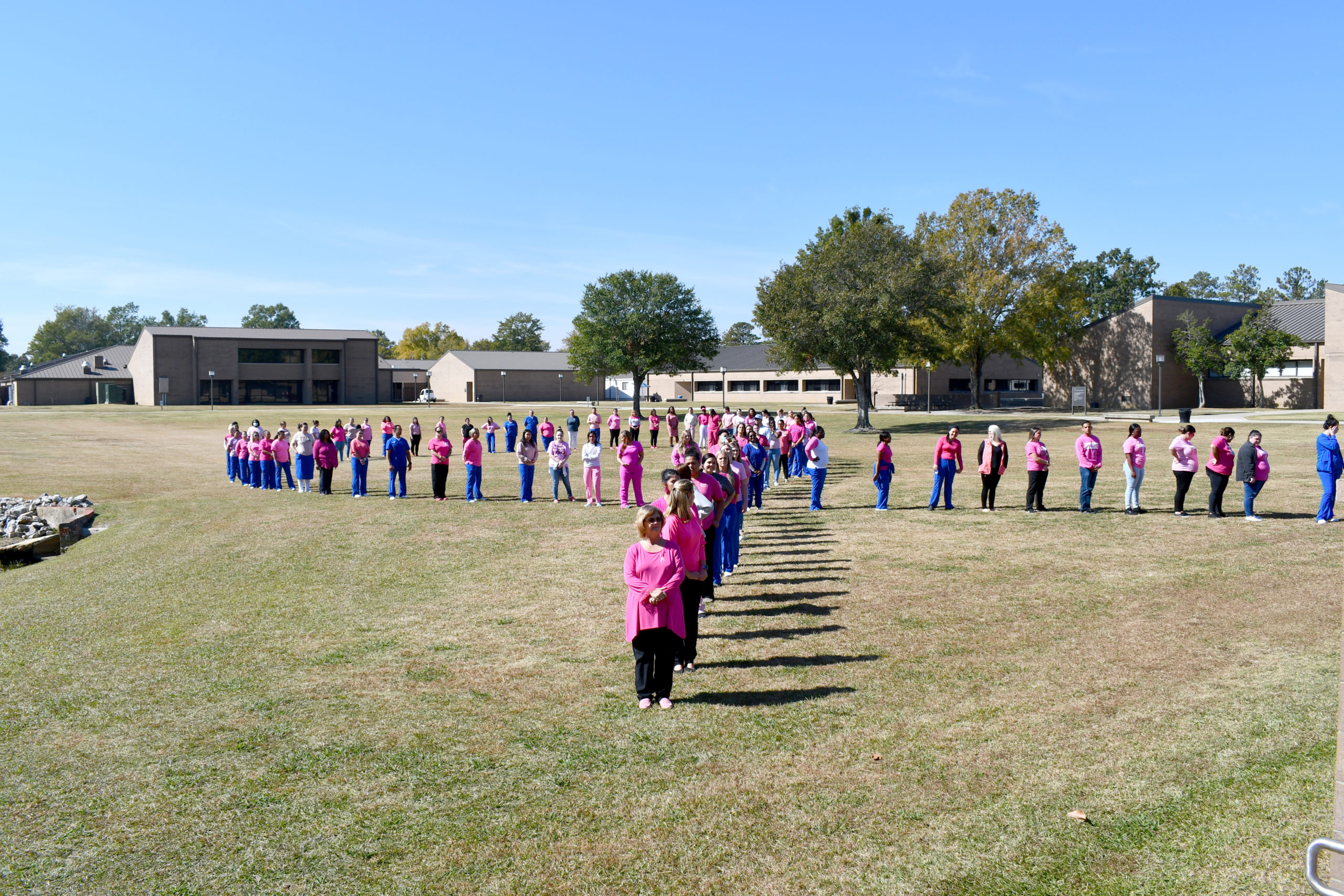 Nursing students stand to make a human pink ribbon in middle of campus