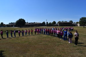 Nursing students stand to make a human pink ribbon in middle of campus