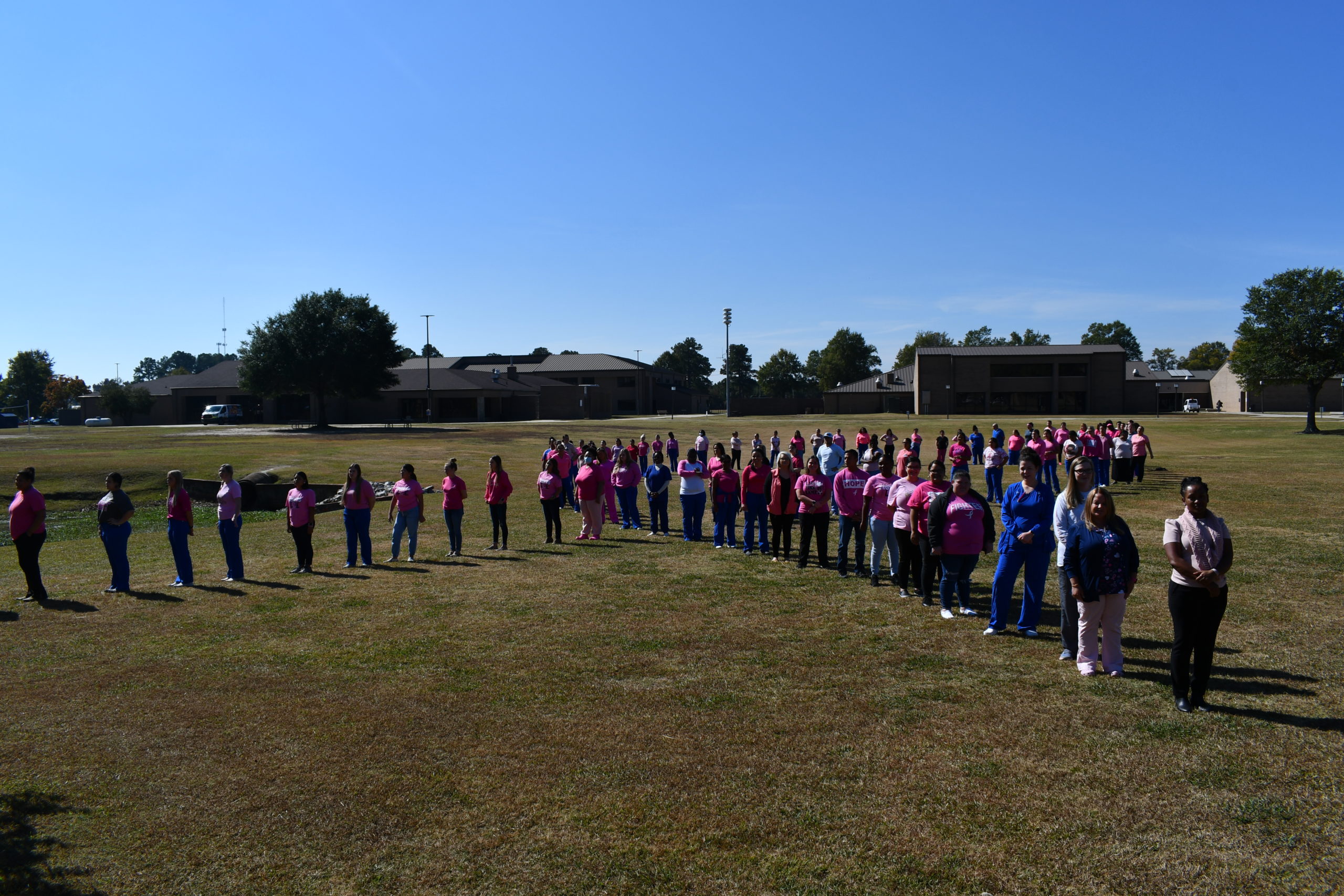 Nursing students stand to make a human pink ribbon in middle of campus
