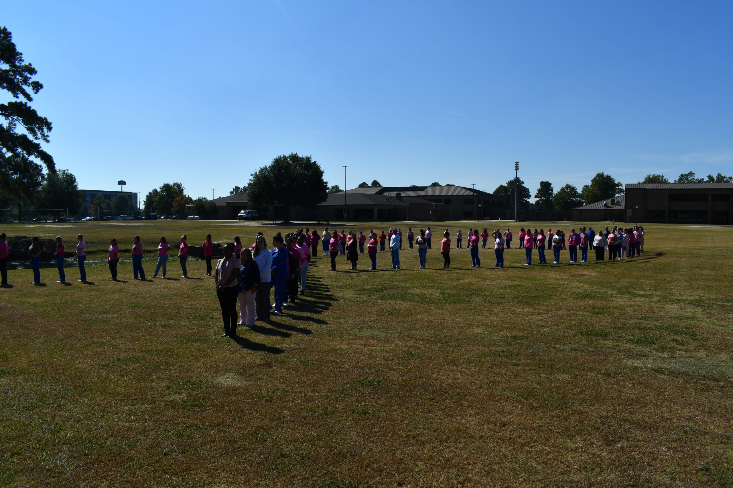 Nursing students stand to make a human pink ribbon in middle of campus