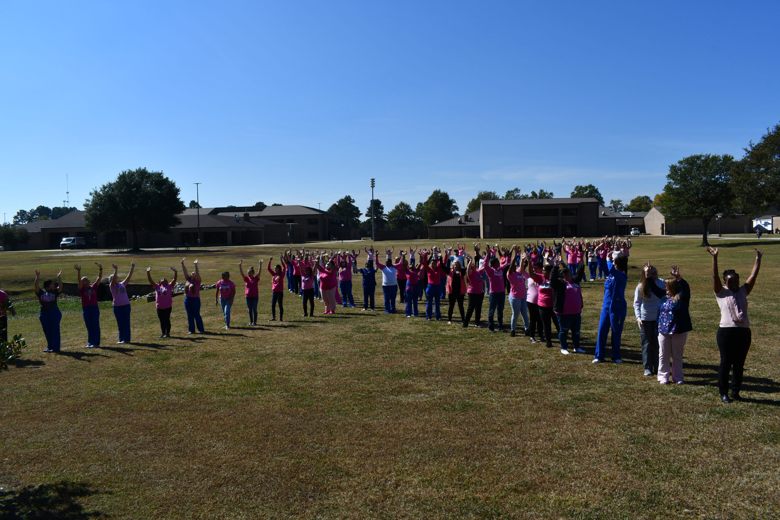 Nursing students stand to make a human pink ribbon in middle of campus