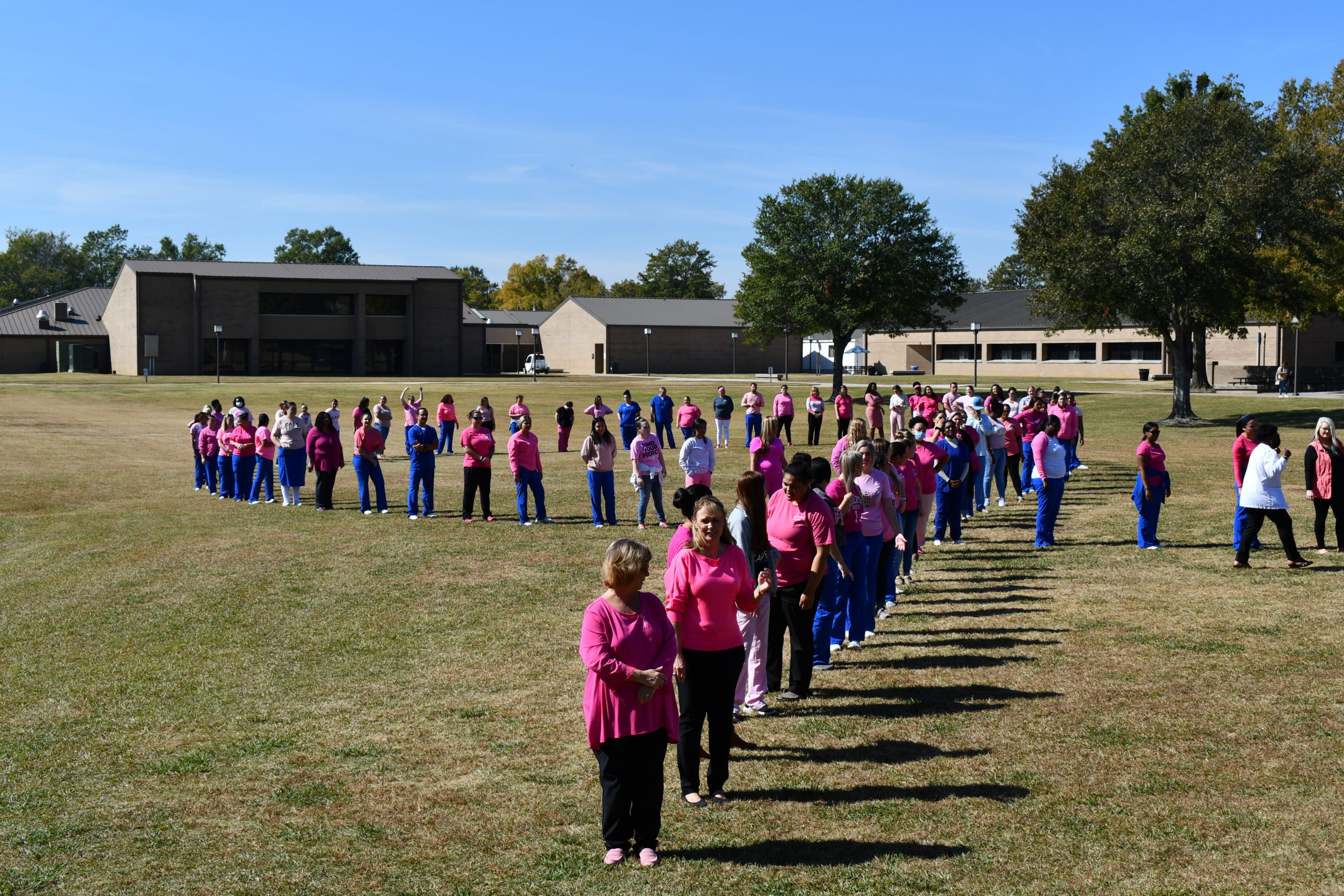 Nursing students stand to make a human pink ribbon in middle of campus