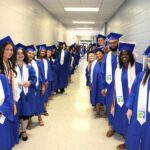 A photo of students lining a hallway on two sides dressed in blue robes with white sashes
