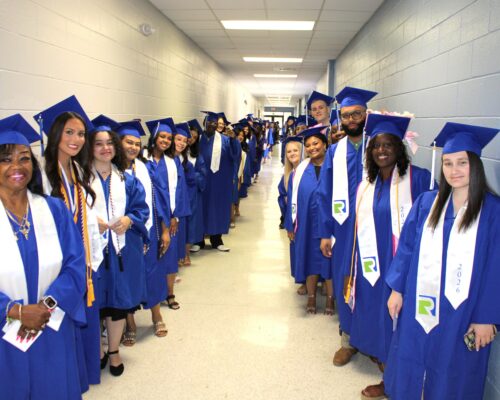 A photo of students lining a hallway on two sides dressed in blue robes with white sashes